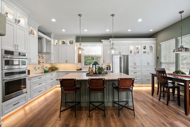 Inspiration for a large transitional l-shaped medium tone wood floor and brown floor open concept kitchen remodel in Other with an undermount sink, recessed-panel cabinets, white cabinets, quartz countertops, beige backsplash, subway tile backsplash, stainless steel appliances, an island and beige countertops