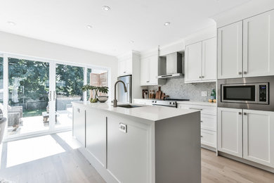 Inspiration for a transitional galley light wood floor and beige floor kitchen remodel in Other with an undermount sink, shaker cabinets, white cabinets, white backsplash, marble backsplash, stainless steel appliances, an island and white countertops