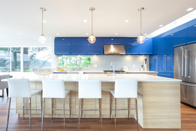 Inspiration for a mid-sized beach style eat-in kitchen in Vancouver with an undermount sink, flat-panel cabinets, blue cabinets, quartz benchtops, ceramic splashback, stainless steel appliances, medium hardwood floors, with island, white benchtop and grey splashback.