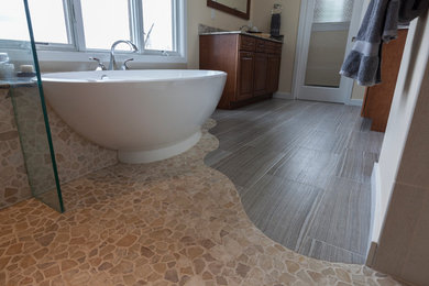 This is an example of a large contemporary master bathroom in Bridgeport with a vessel sink, raised-panel cabinets, medium wood cabinets, a freestanding tub, an open shower, a two-piece toilet, beige tile, porcelain tile, beige walls and porcelain floors.