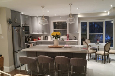 This is an example of a contemporary l-shaped eat-in kitchen in Toronto with a single-bowl sink, raised-panel cabinets, grey cabinets, quartzite benchtops, white splashback, glass tile splashback, stainless steel appliances, porcelain floors, with island and grey floor.