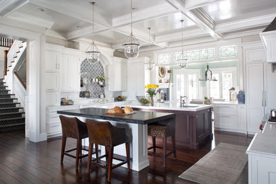 Expansive traditional u-shaped open plan kitchen in Denver with a farmhouse sink, beaded inset cabinets, white cabinets, marble benchtops, dark hardwood floors, multiple islands and grey splashback.