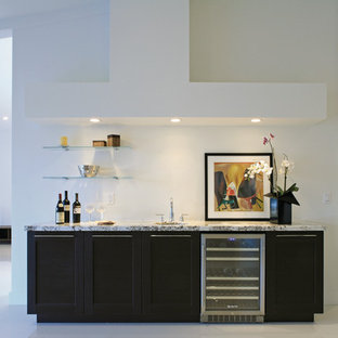 ニューヨークの大きいモダンスタイルのおしゃれなウェットバー (濃色木目調キャビネット、白いキッチンパネル、アンダーカウンターシンク、御影石カウンター、コンクリートの床、シェーカースタイル扉のキャビネット、グレーのキッチンカウンター) の写真