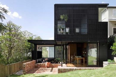 This is an example of a contemporary two-storey black exterior in Brisbane with wood siding and a flat roof.