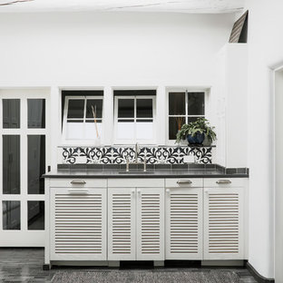 サンタフェスタイルのおしゃれなウェットバー (ルーバー扉のキャビネット、白いキャビネット、マルチカラーのキッチンパネル、黒い床、黒いキッチンカウンター) の写真