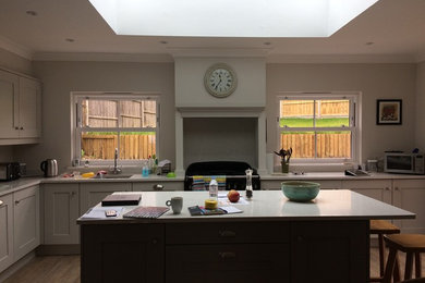 Elegant laminate floor kitchen photo in Surrey with a drop-in sink, shaker cabinets, solid surface countertops, stainless steel appliances and an island