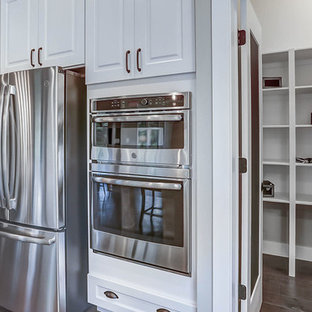 Lantlig inredning av ett mycket stort grå grått kök, med en rustik diskho, vita skåp, bänkskiva i kvarts, grått stänkskydd, rostfria vitvaror, mellanmörkt trägolv och en köksö