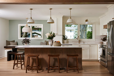 Example of a transitional l-shaped medium tone wood floor and brown floor kitchen design in Minneapolis with an undermount sink, recessed-panel cabinets, white cabinets, gray backsplash, stainless steel appliances, an island and white countertops