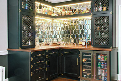 Inspiration for a small l-shaped dry bar remodel in Other with recessed-panel cabinets, brown cabinets, wood countertops, mirror backsplash and brown countertops