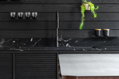 Mid-sized industrial single-wall kitchen in Montreal with an undermount sink, louvered cabinets, black cabinets, marble benchtops, black splashback, timber splashback, panelled appliances, concrete floors, with island, beige floor and black benchtop.