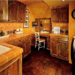 Mediterranean utility room in Orange County with a submerged sink, raised-panel cabinets, distressed cabinets, tile countertops, terracotta flooring, a side by side washer and dryer, orange worktops and orange walls.