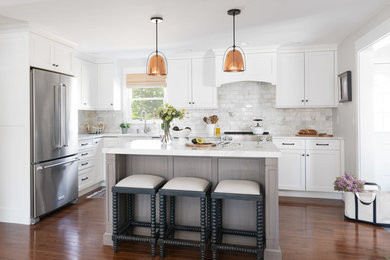 Design ideas for a beach style l-shaped kitchen in Boston with shaker cabinets, white cabinets, quartz benchtops, white splashback, marble splashback, stainless steel appliances, medium hardwood floors, brown floor, white benchtop and with island.