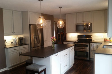 Example of an u-shaped vinyl floor and brown floor kitchen design in Cleveland with an undermount sink, raised-panel cabinets, white cabinets, granite countertops, white backsplash, glass tile backsplash, stainless steel appliances, an island and black countertops