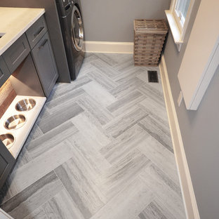 シャーロットの中サイズのカントリー風おしゃれな洗濯室 (アンダーカウンターシンク、シェーカースタイル扉のキャビネット、グレーのキャビネット、クオーツストーンカウンター、ライムストーンの床、上下配置の洗濯機・乾燥機、グレーの壁) の写真