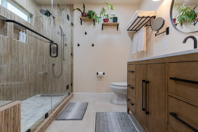Example of a mid-sized minimalist 3/4 ceramic tile and multicolored tile single-sink, ceramic tile, multicolored floor and brick wall bathroom design in Phoenix with shaker cabinets, brown cabinets, quartz countertops, white countertops, a built-in vanity, a one-piece toilet, an undermount sink, a hinged shower door and white walls