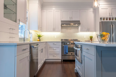 Example of a mid-sized minimalist l-shaped dark wood floor and brown floor open concept kitchen design in New York with a drop-in sink, recessed-panel cabinets, white cabinets, quartzite countertops, white backsplash, glass tile backsplash, stainless steel appliances, an island and white countertops