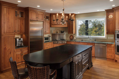 Example of a large classic u-shaped medium tone wood floor and brown floor kitchen design in Atlanta with an undermount sink, raised-panel cabinets, distressed cabinets, quartzite countertops, stainless steel appliances, an island and black countertops