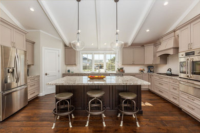 Photo of a mid-sized transitional u-shaped eat-in kitchen in Santa Barbara with an undermount sink, recessed-panel cabinets, beige cabinets, granite benchtops, white splashback, subway tile splashback, stainless steel appliances, dark hardwood floors, with island, brown floor and multi-coloured benchtop.