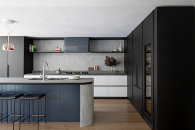Inspiration for a large contemporary l-shaped open plan kitchen in Sydney with a double-bowl sink, flat-panel cabinets, concrete benchtops, grey splashback, porcelain splashback, black appliances, medium hardwood floors, with island and grey benchtop.