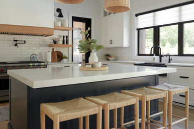 Large cottage u-shaped light wood floor, beige floor and exposed beam eat-in kitchen photo in Toronto with a farmhouse sink, flat-panel cabinets, white cabinets, white backsplash, subway tile backsplash, stainless steel appliances, an island and white countertops