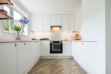 Photo of a small contemporary u-shaped kitchen/diner in Other with a double-bowl sink, flat-panel cabinets, white cabinets, composite countertops, white splashback, integrated appliances, no island and white worktops.