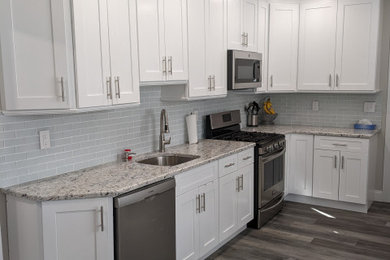 Inspiration for a transitional laminate floor and brown floor kitchen remodel in New York with an undermount sink, shaker cabinets, white cabinets, granite countertops, white backsplash, stainless steel appliances and white countertops