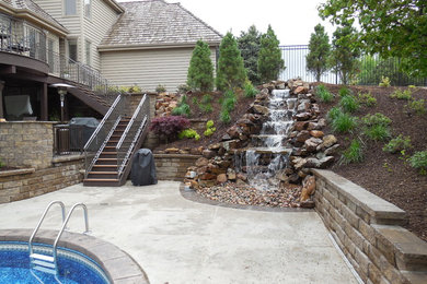 This is an example of a large traditional backyard custom-shaped lap pool in Omaha with a water feature and concrete pavers.