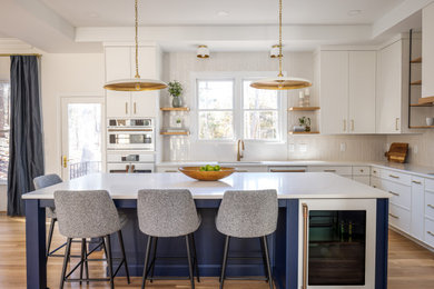 Inspiration for a transitional open plan kitchen in Raleigh with an undermount sink, white cabinets, quartzite benchtops, white splashback, porcelain splashback, white appliances, medium hardwood floors, with island, brown floor, white benchtop and recessed.
