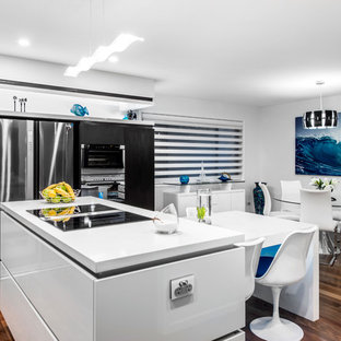 Inredning av ett modernt mellanstort kök, med en undermonterad diskho, släta luckor, turkosa skåp, bänkskiva i kvarts, svarta vitvaror, mellanmörkt trägolv och en köksö