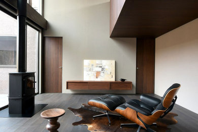 Modelo de salón abierto y gris retro de tamaño medio con paredes grises, suelo de madera oscura, estufa de leña, marco de chimenea de metal, televisor colgado en la pared, suelo negro y madera