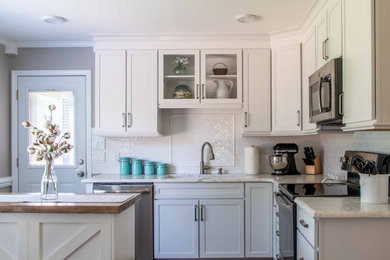 Example of a small transitional u-shaped vinyl floor and brown floor enclosed kitchen design in Raleigh with a double-bowl sink, shaker cabinets, white cabinets, quartz countertops, white backsplash, subway tile backsplash, stainless steel appliances, an island and white countertops