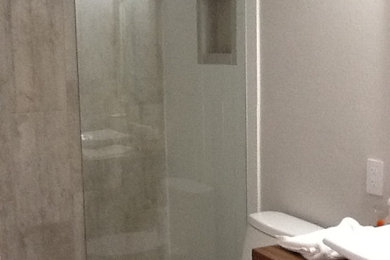Bathroom - small modern gray tile and ceramic tile ceramic tile, gray floor and single-sink bathroom idea in Other with open cabinets, brown cabinets, a one-piece toilet, gray walls, a vessel sink, wood countertops, brown countertops and a built-in vanity