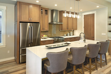 Inspiration for a mid-sized transitional single-wall open plan kitchen in Sacramento with a farmhouse sink, recessed-panel cabinets, light wood cabinets, solid surface benchtops, brown splashback, glass tile splashback, stainless steel appliances, medium hardwood floors, with island, brown floor and white benchtop.