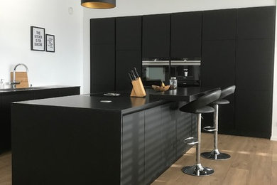 Inspiration for a mid-sized contemporary l-shaped open plan kitchen in Other with a drop-in sink, flat-panel cabinets, black cabinets, black appliances, painted wood floors, a peninsula and brown floor.