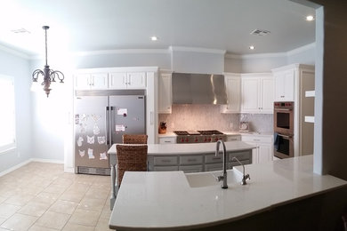 Large trendy u-shaped porcelain tile and beige floor eat-in kitchen photo in Oklahoma City with a farmhouse sink, raised-panel cabinets, white cabinets, quartz countertops, gray backsplash, mosaic tile backsplash, stainless steel appliances, an island and white countertops