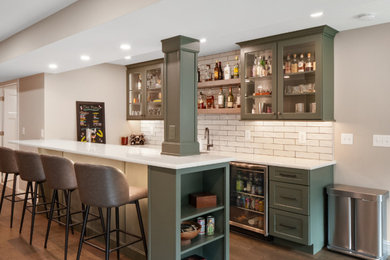 Brown floor home bar photo in St Louis with green cabinets, white backsplash and white countertops