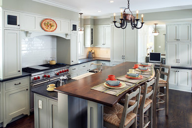 Inspiration for a traditional l-shaped kitchen in Minneapolis with a farmhouse sink, shaker cabinets, green cabinets, soapstone benchtops, white splashback, subway tile splashback, stainless steel appliances, dark hardwood floors and with island.