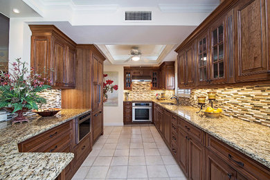 Large galley porcelain tile and beige floor enclosed kitchen photo in Other with a double-bowl sink, raised-panel cabinets, dark wood cabinets, granite countertops, multicolored backsplash, matchstick tile backsplash, stainless steel appliances and a peninsula