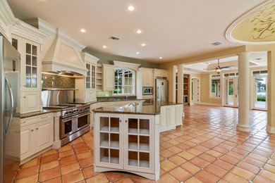 Inspiration for a large mediterranean u-shaped terra-cotta tile open concept kitchen remodel in Orlando with an undermount sink, raised-panel cabinets, granite countertops, green backsplash, stainless steel appliances and an island