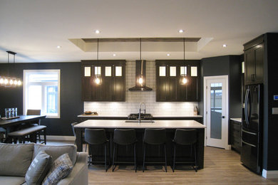 Transitional l-shaped open concept kitchen photo in Toronto with shaker cabinets, dark wood cabinets, quartz countertops, white backsplash, ceramic backsplash, black appliances, an island and white countertops