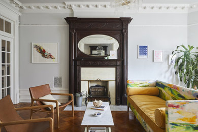 Пример оригинального дизайна: изолированная гостиная комната среднего размера в стиле фьюжн с серыми стенами, паркетным полом среднего тона, стандартным камином, фасадом камина из плитки и коричневым полом без телевизора