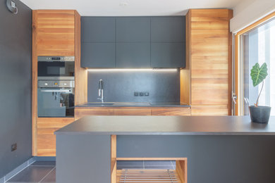 Inspiration for a medium sized modern galley open plan kitchen in Paris with an integrated sink, flat-panel cabinets, medium wood cabinets, engineered stone countertops, black splashback, engineered quartz splashback, integrated appliances, an island, black floors and black worktops.