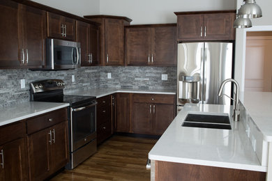 Mid-sized transitional l-shaped dark wood floor enclosed kitchen photo in Other with a double-bowl sink, shaker cabinets, dark wood cabinets, quartz countertops, gray backsplash, stone tile backsplash, stainless steel appliances and an island