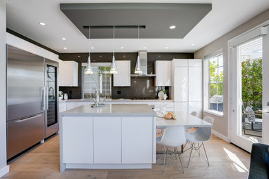 Inspiration for a mid-sized modern l-shaped light wood floor and tray ceiling open concept kitchen remodel in San Francisco with an undermount sink, flat-panel cabinets, white cabinets, quartz countertops, gray backsplash, quartz backsplash, stainless steel appliances, an island and gray countertops