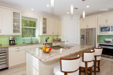 Mid-sized beach style u-shaped light wood floor and beige floor eat-in kitchen photo in Miami with a double-bowl sink, raised-panel cabinets, white cabinets, laminate countertops, green backsplash, stainless steel appliances and an island