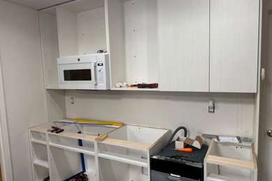 Example of a mid-sized beach style galley gray floor eat-in kitchen design in New York with an undermount sink, flat-panel cabinets, white cabinets, solid surface countertops, white backsplash, subway tile backsplash, paneled appliances and turquoise countertops