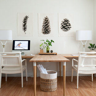 Klassisk inredning av ett mellanstort hemmabibliotek, med vita väggar, mellanmörkt trägolv, ett fristående skrivbord och beiget golv