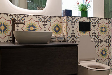 This is an example of a small mediterranean cloakroom in Manchester with flat-panel cabinets, dark wood cabinets, a wall mounted toilet, multi-coloured tiles, porcelain tiles, beige walls, porcelain flooring, a pedestal sink, wooden worktops, multi-coloured floors, brown worktops and a freestanding vanity unit.