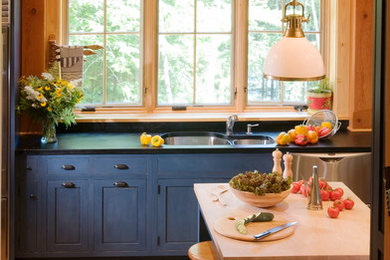 Enclosed kitchen - mid-sized craftsman u-shaped medium tone wood floor enclosed kitchen idea in Portland Maine with a double-bowl sink, shaker cabinets, blue cabinets, soapstone countertops, multicolored backsplash, stone tile backsplash, stainless steel appliances and an island