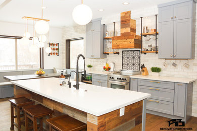 Inspiration for a mid-sized cottage l-shaped medium tone wood floor and brown floor eat-in kitchen remodel in Salt Lake City with a farmhouse sink, shaker cabinets, gray cabinets, quartz countertops, white backsplash, mosaic tile backsplash, stainless steel appliances, an island and white countertops